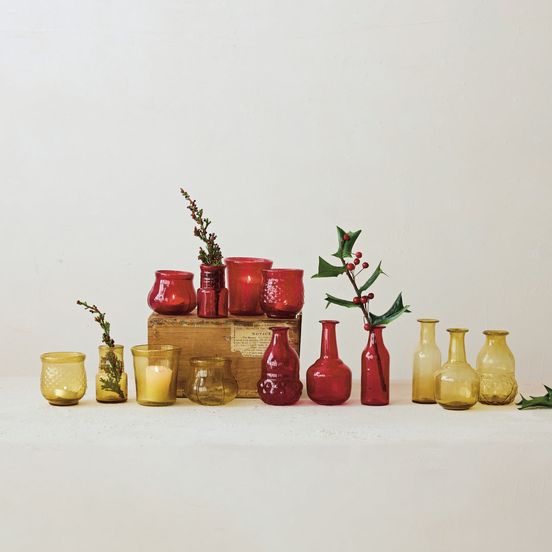 A collection of hand-blown red and amber glass bud vases and candle holders on a white surface.