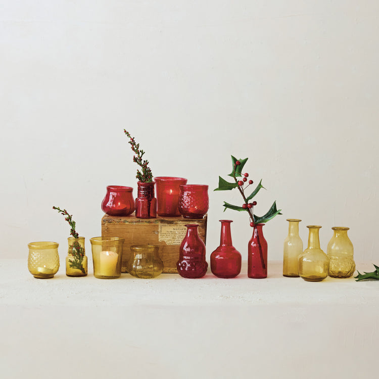 A collection of hand-blown red and amber glass bud vases and candle holders on a white surface.