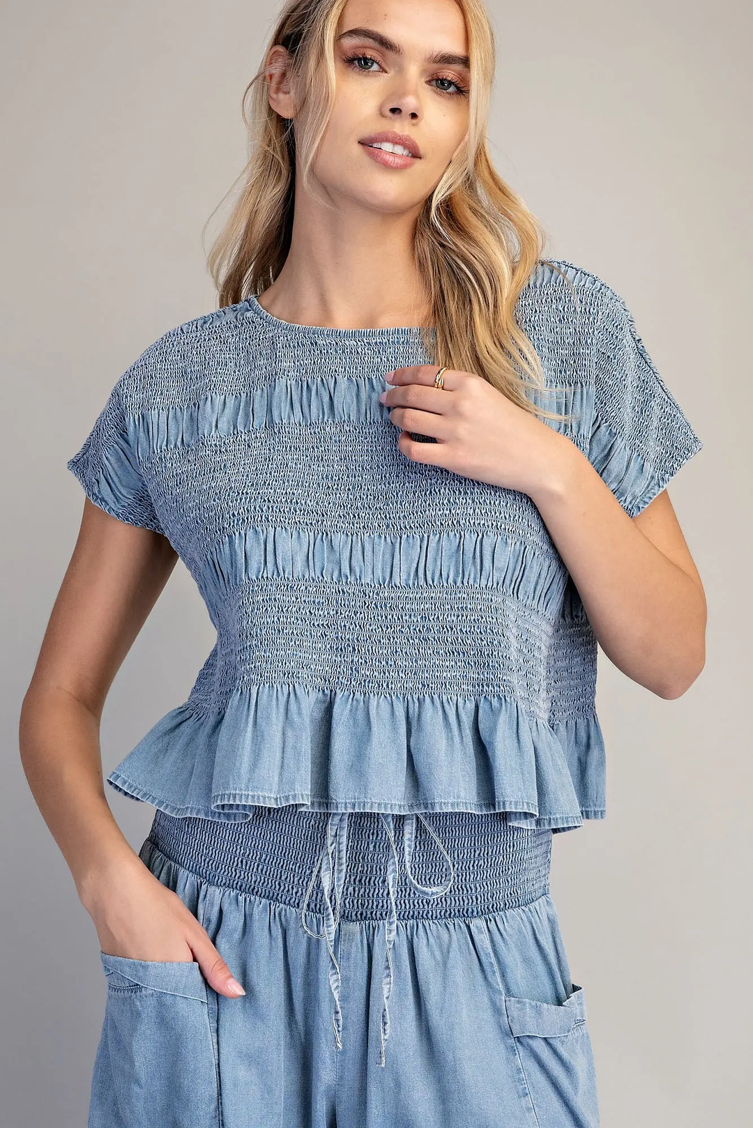 Woman wearing a blue mineral washed smocked cap sleeve top with a ruffled hem.