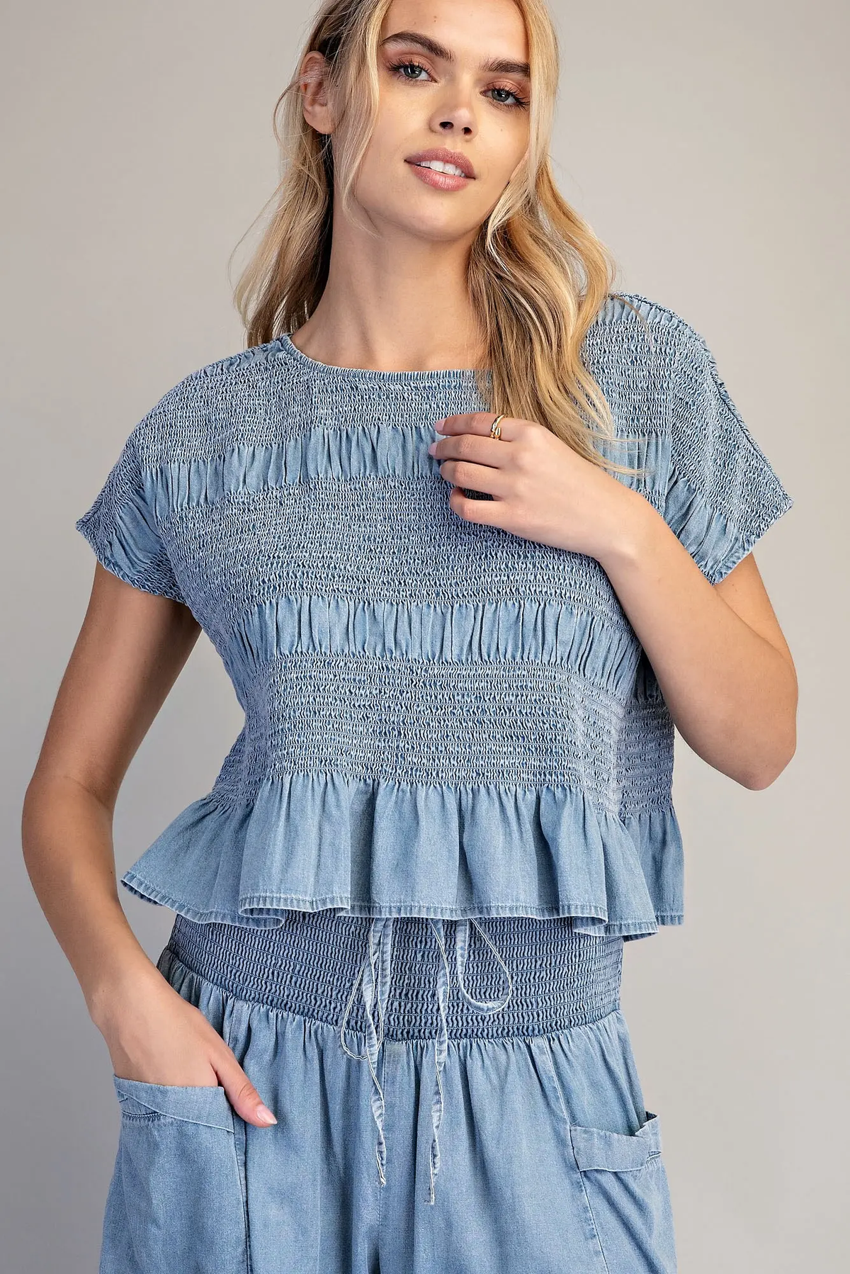 Woman wearing a blue mineral washed smocked cap sleeve top with a ruffled hem.