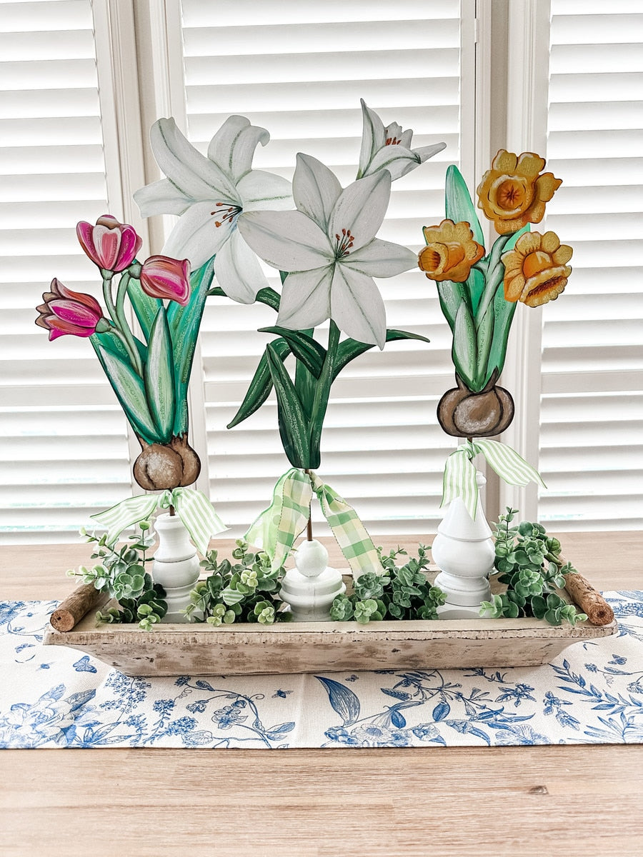Wooden cutout spring flowers: tulips, lilies, and daffodils with bulbs and green ribbon accents.