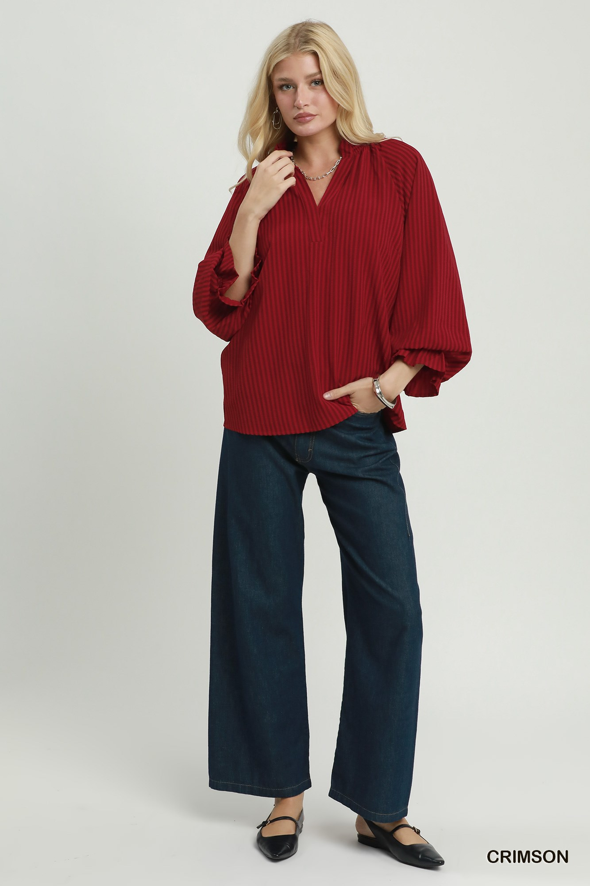 Woman wearing the Emma Stripe Split Neck Blouse in crimson with dark wide-leg jeans.