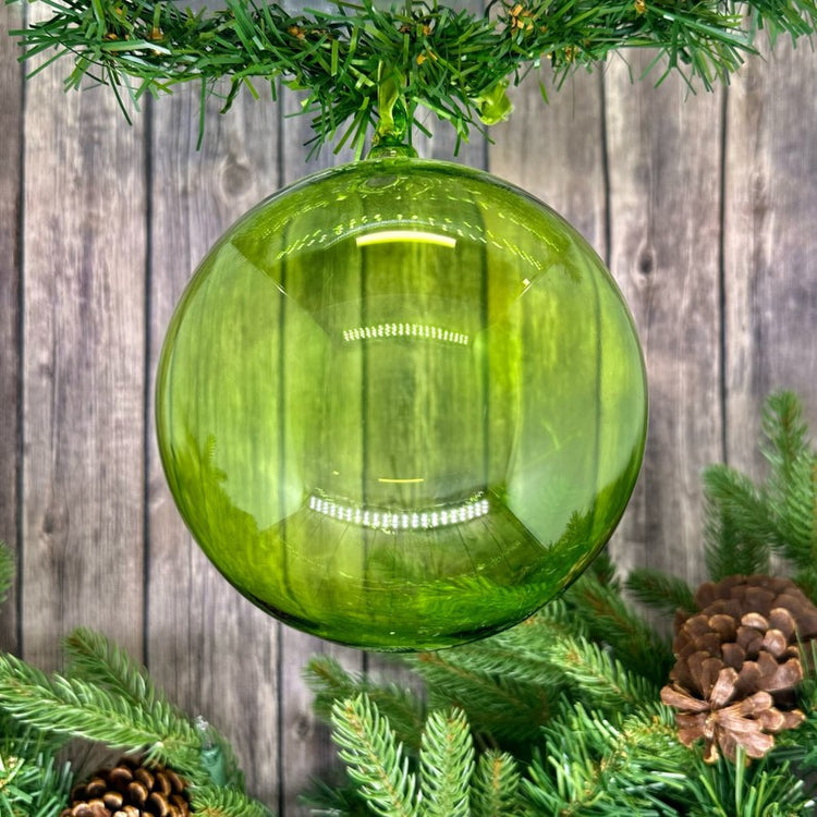 Large 150mm hand-blown lime green glass ball ornament hanging from a pine branch.