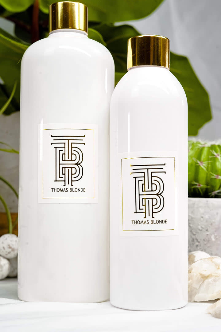 Two white bottles of Thomas Blonde Diffusing Oil with gold caps and labels on a white surface.