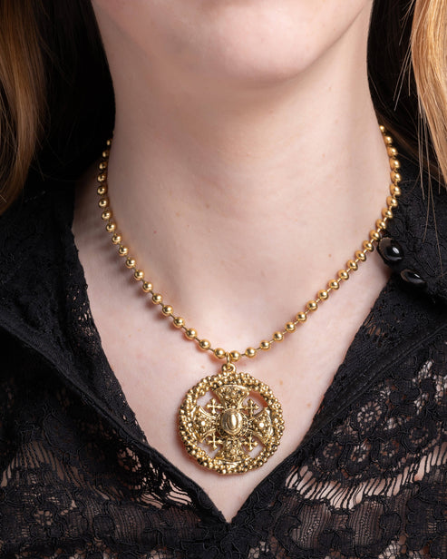 Joy Necklace featuring a gold ball chain and a circular ornate cross pendant on a person.