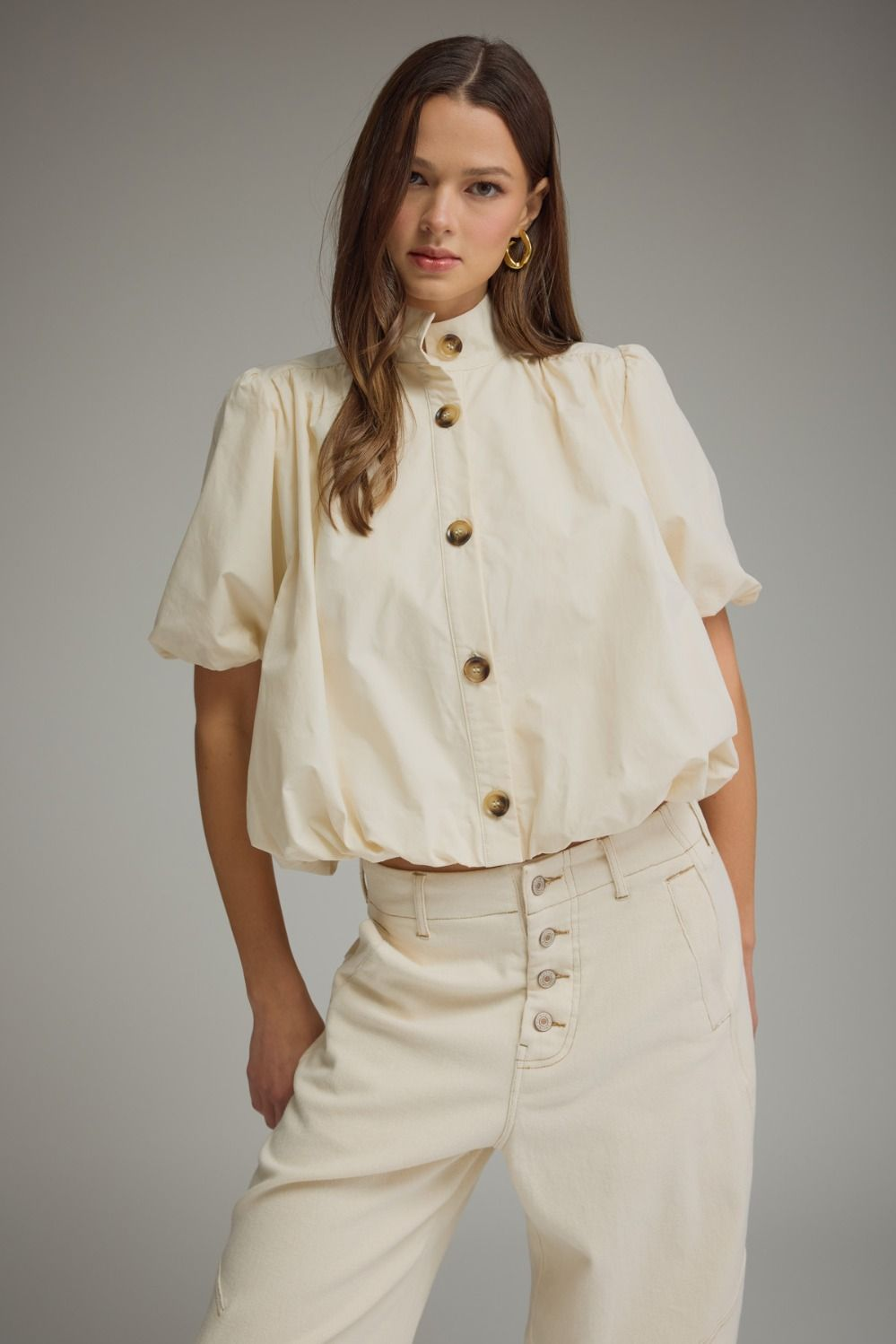 Woman wearing the Jacky cream short puff sleeve top with a bubble hem and band collar.
