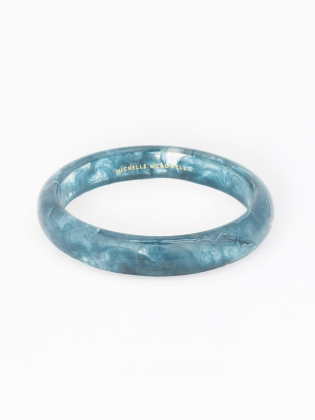 Betty Bangle, a blue marbled resin bracelet with gold Michelle McDowell branding on the interior.
