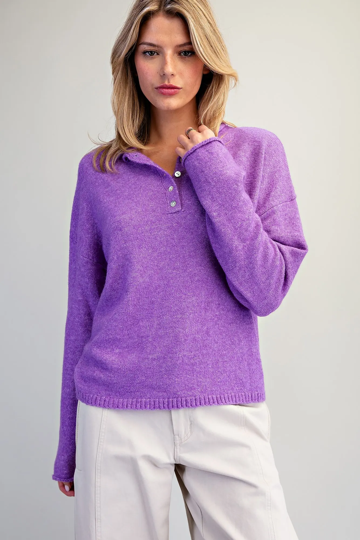 Woman wearing a purple Donna long sleeve knit sweater with a buttoned polo collar and white pants.