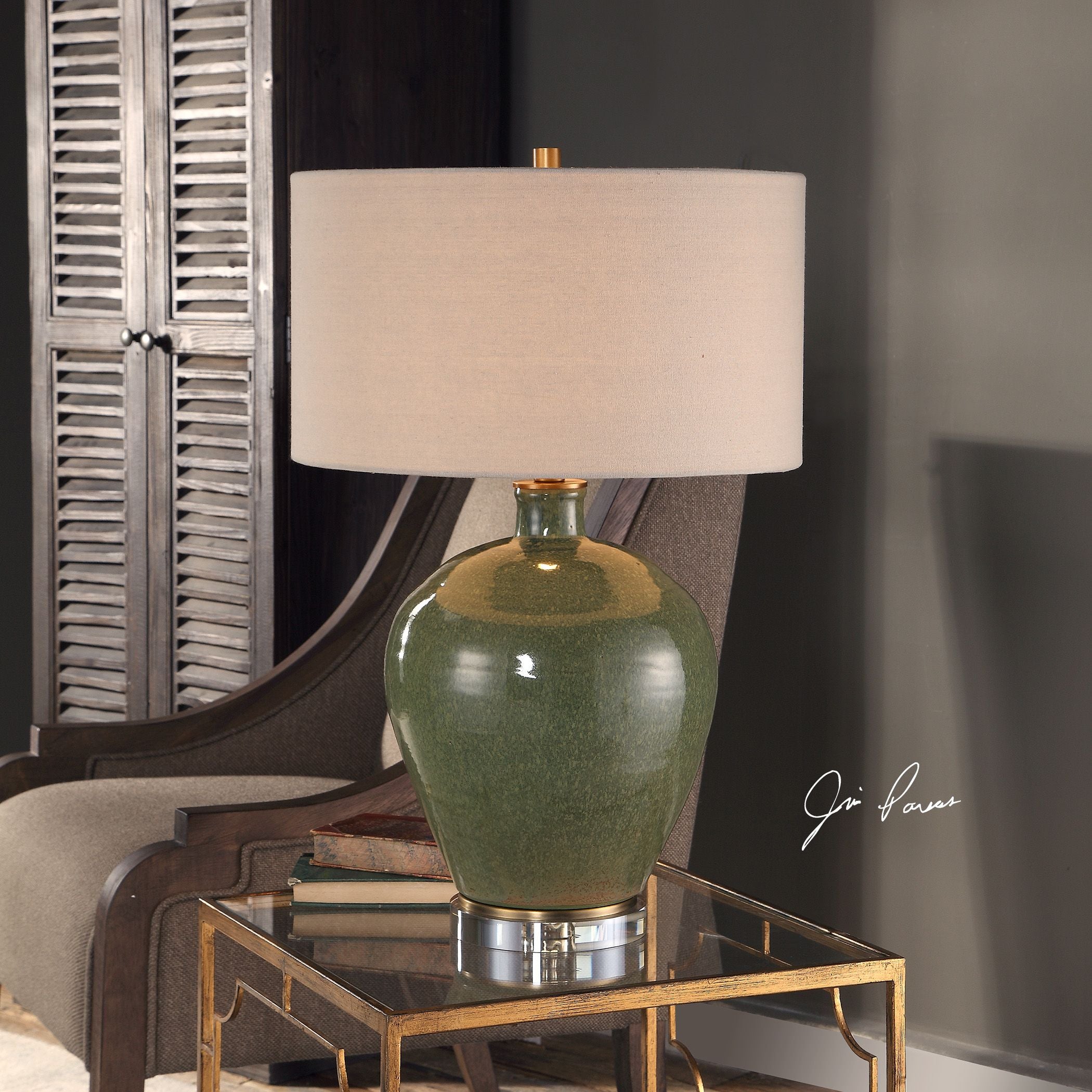 Elva table lamp with distressed emerald green ceramic base, antique brass accents, crystal foot, and beige linen drum shade.