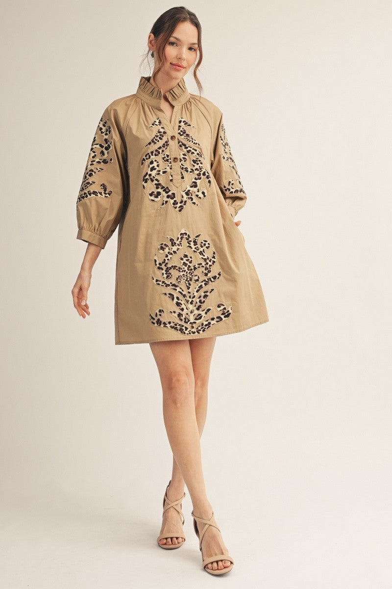 Woman wearing a tan mini dress with leopard print baroque applique details and ruffled collar.