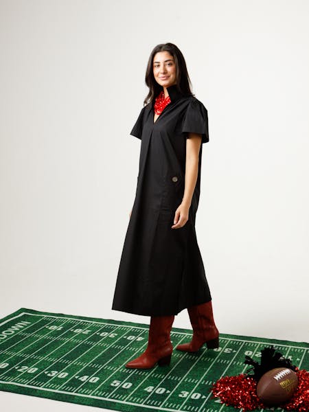 Woman wearing a black Gretchen Dress with a stand collar, red necklace, and red boots.