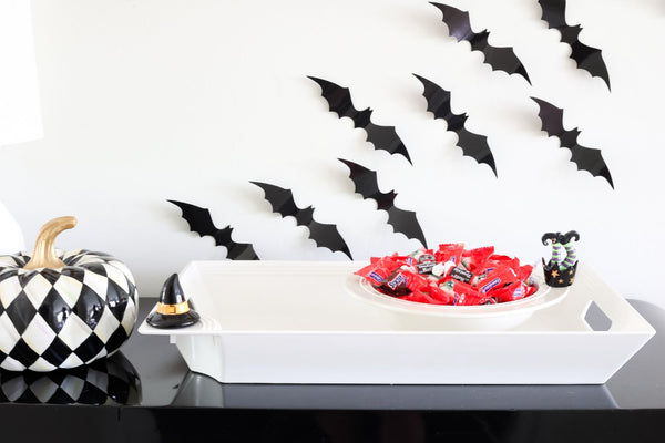 Black and white harlequin pumpkin with gold stem next to a white tray with candy and witch legs decor.