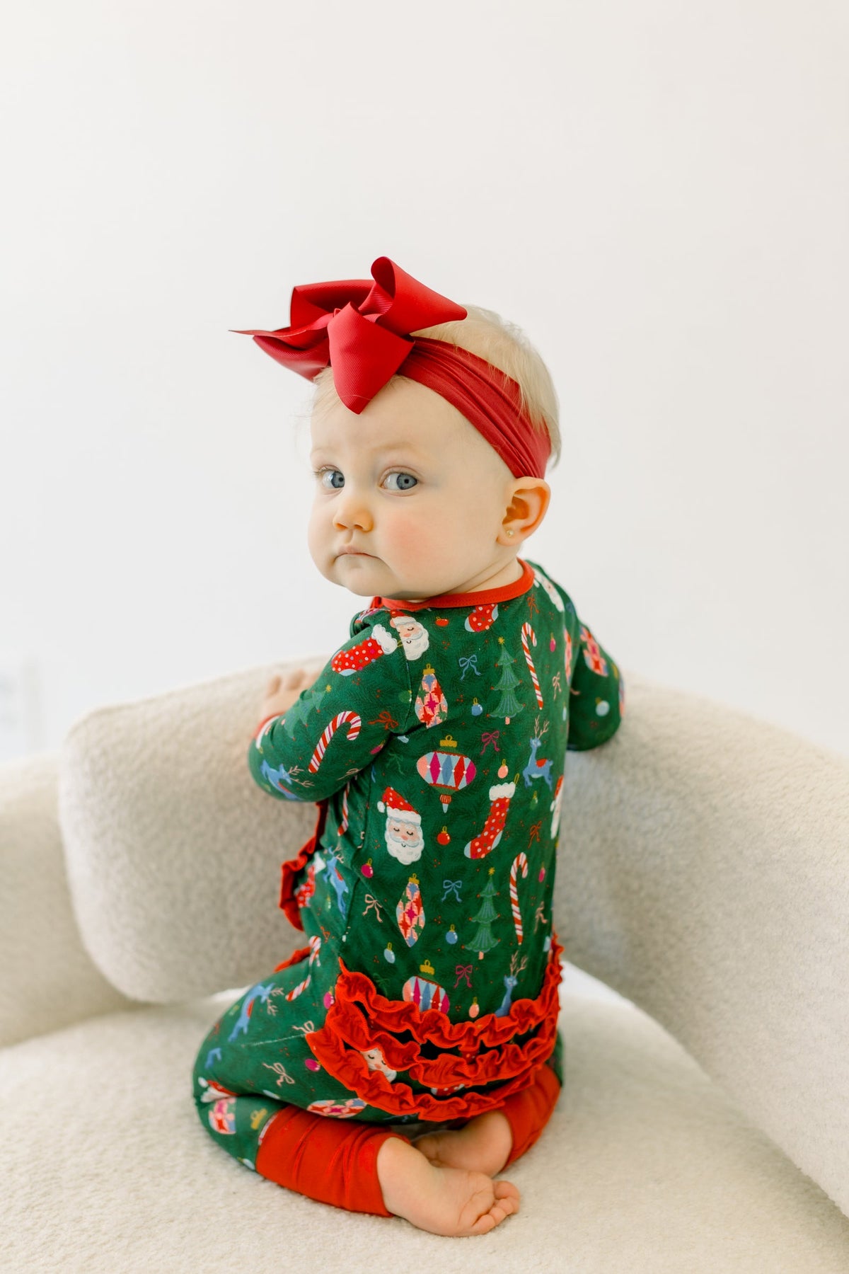 Green bamboo viscose zippy pajamas with a red bow headband, featuring a festive Christmas pattern of Santa, reindeer, and ornaments.