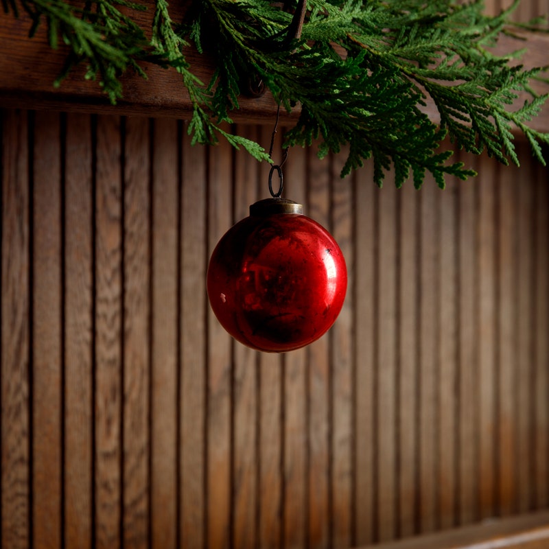 Vintage 3-inch red glass ball ornament with an antique finish hanging from a green cedar branch.