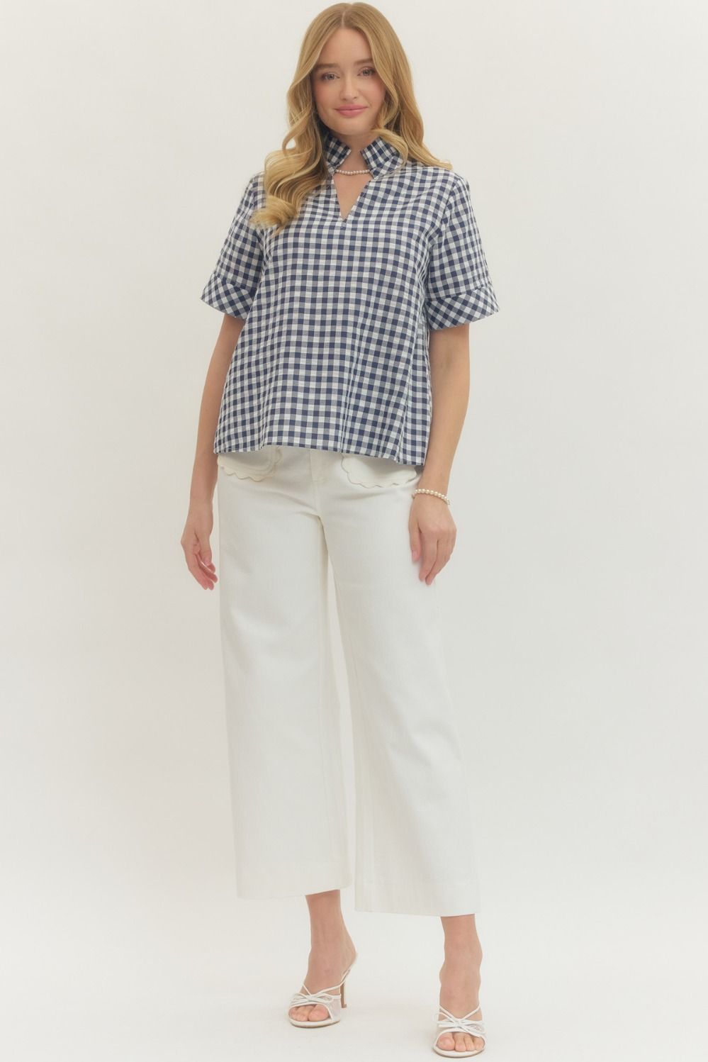 Woman wearing a Natalie Gingham Short Sleeve Top with a stand collar V-neck and white wide-leg pants.