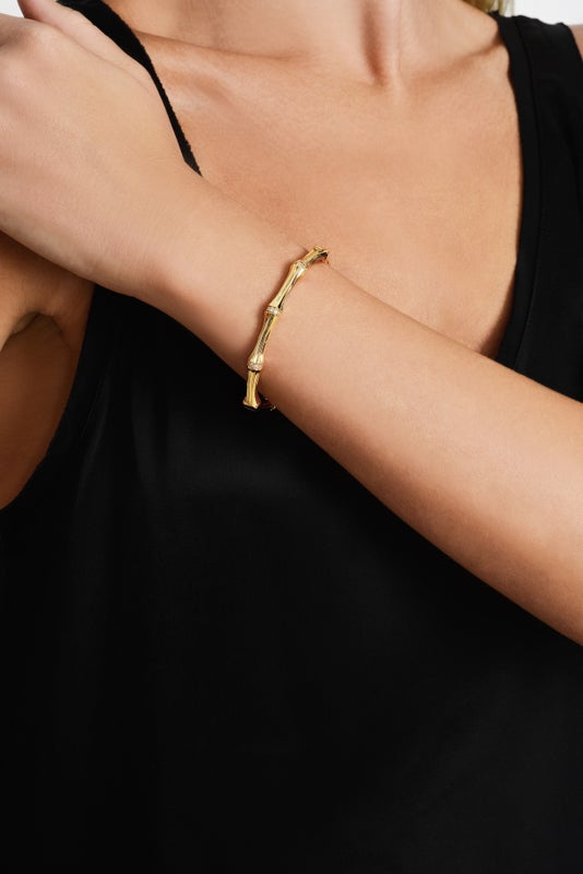 A woman wearing a gold-plated bamboo-shaped hinged bangle with crystal pavé accents on her wrist.