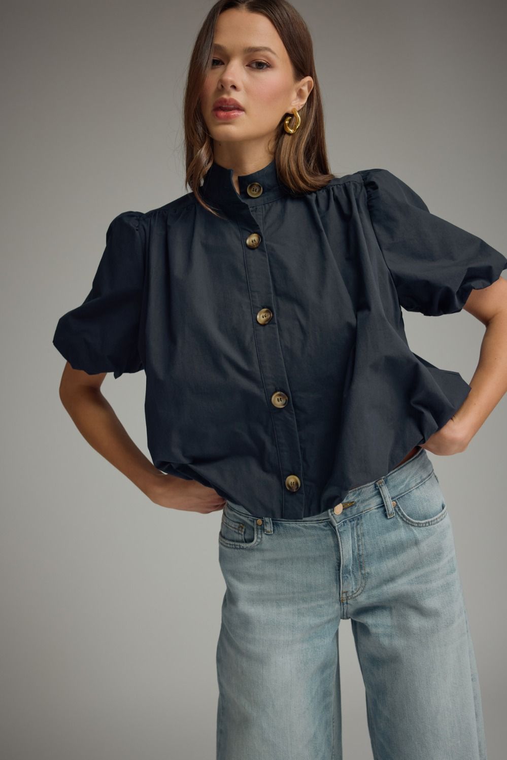 Woman wearing a navy blue Jacky short puff sleeve top with a band collar and light wash jeans.
