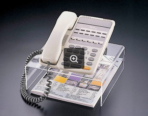 Clear acrylic telephone stand holding a white phone and brochures. The stand elevates the phone for better visibility.