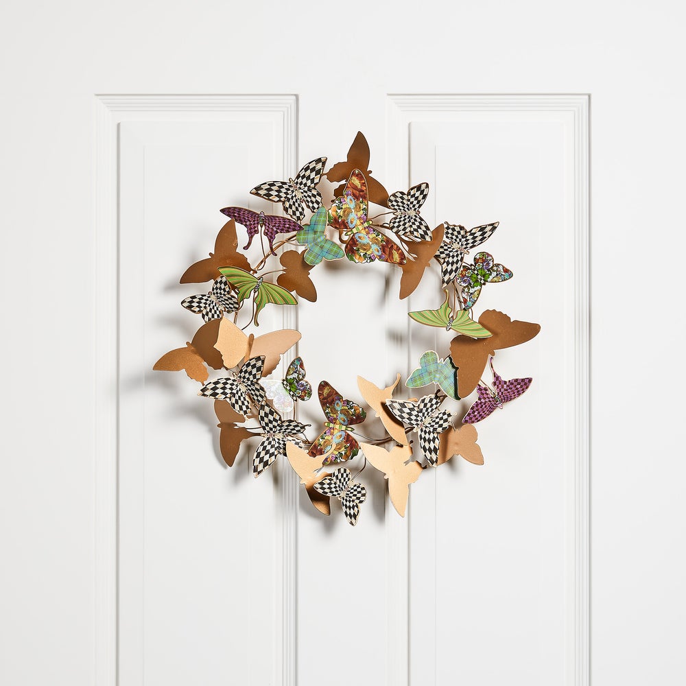 A circular metal wreath featuring colorful patterned and solid gold-tone butterflies on a white door.