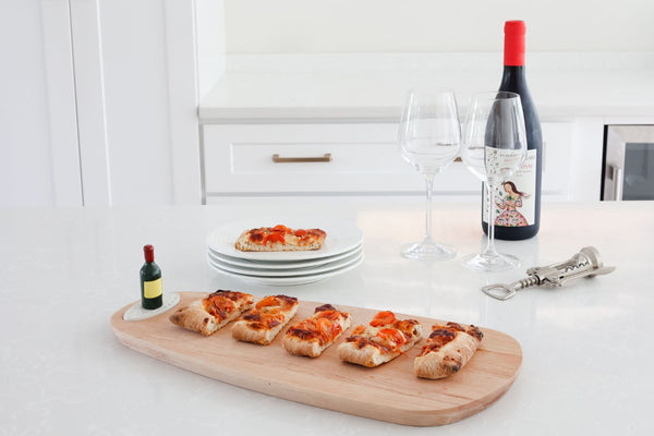Wooden serving board with a miniature wine bottle accent, featuring flatbread slices and wine.
