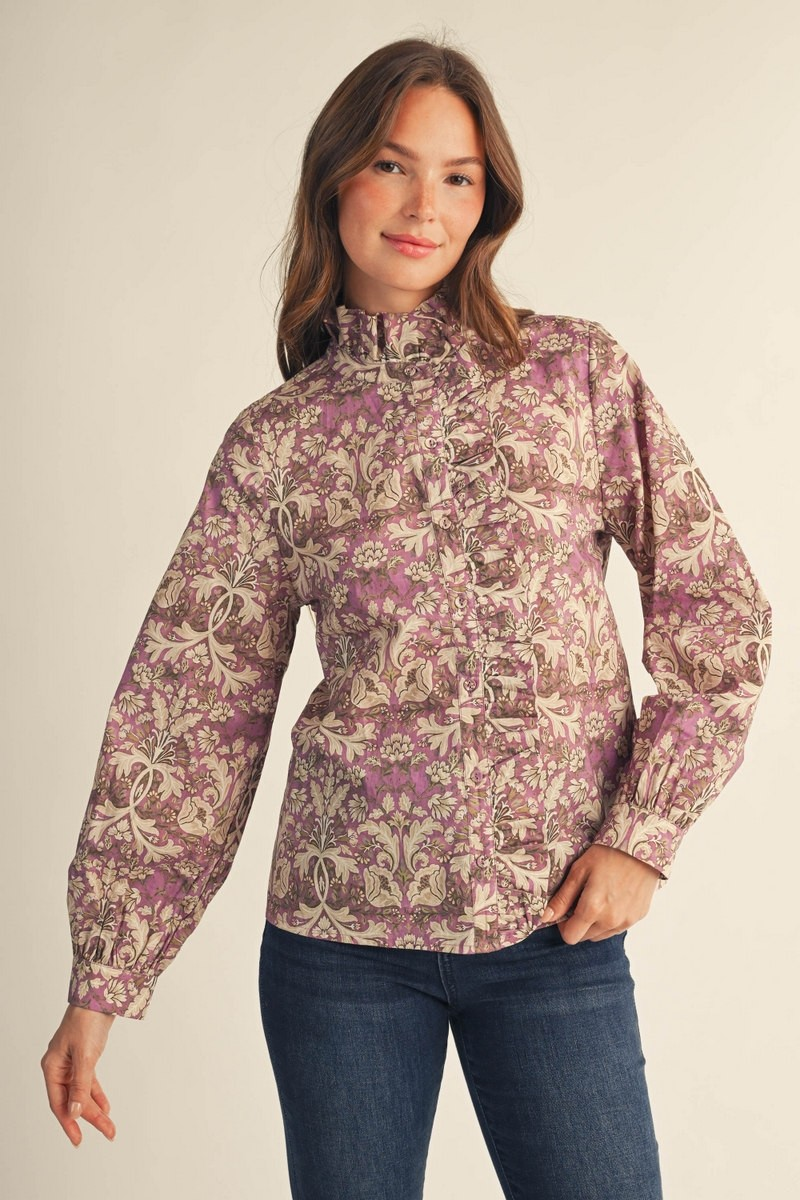 Woman wearing a purple baroque floral print button-down blouse with ruffle details and high neck.