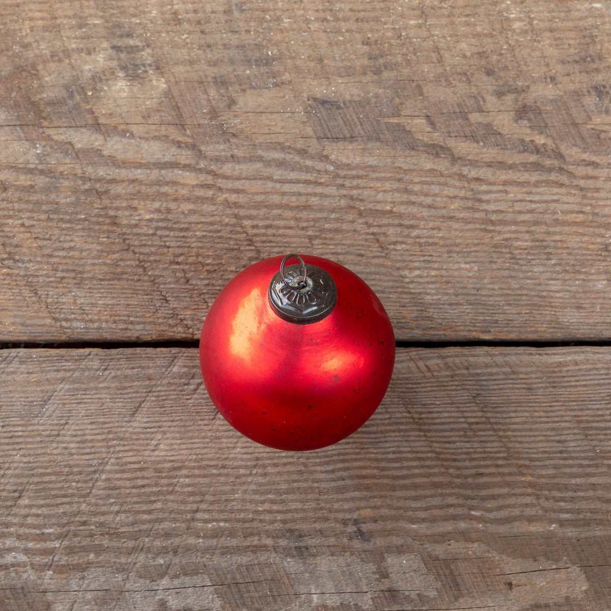 Antique matte ruby glass ball ornament on a rustic wooden surface.