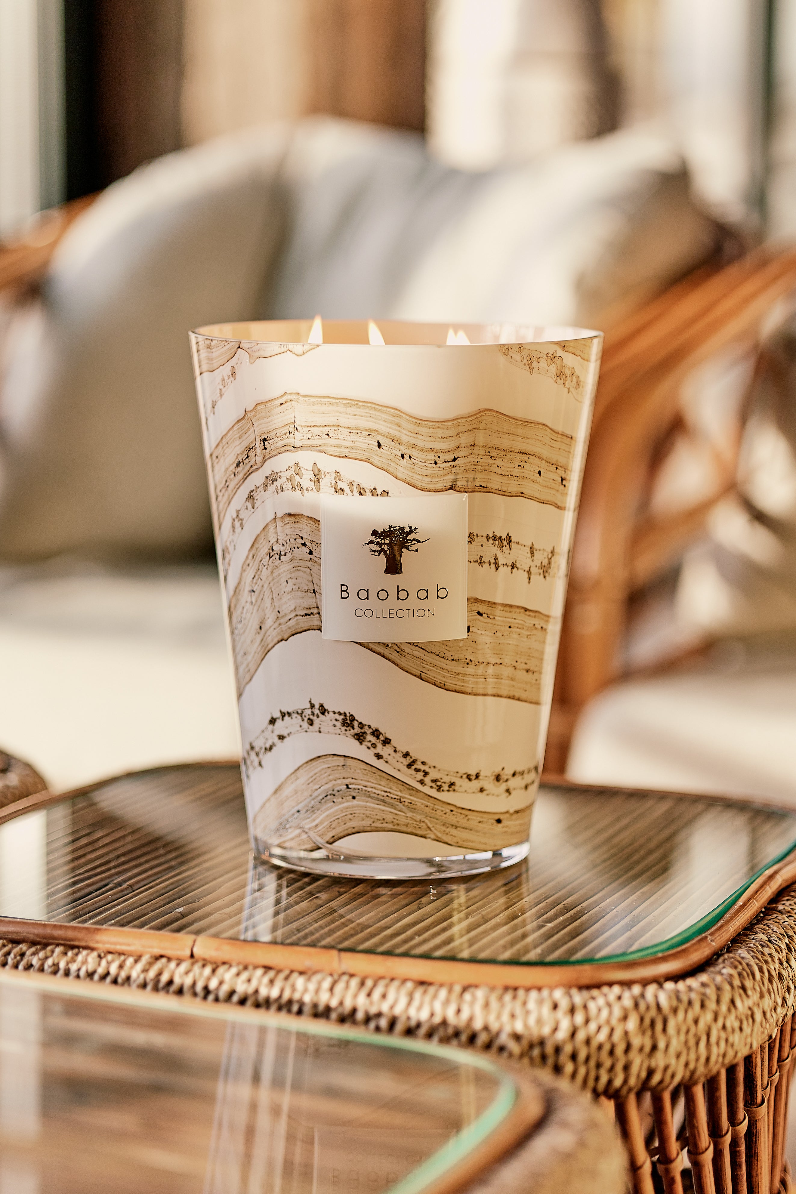 Baobab Collection Sand Siloli candle with beige and brown wavy patterns on a glass table.