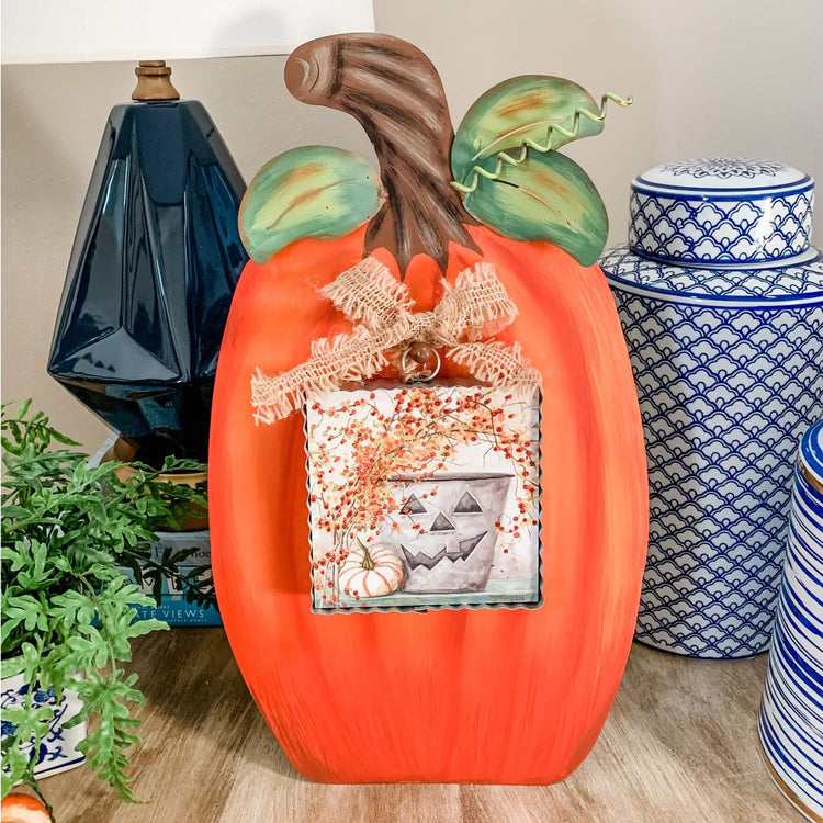 Orange metal display pumpkin with a burlap bow and a small jack-o'-lantern bucket illustration.