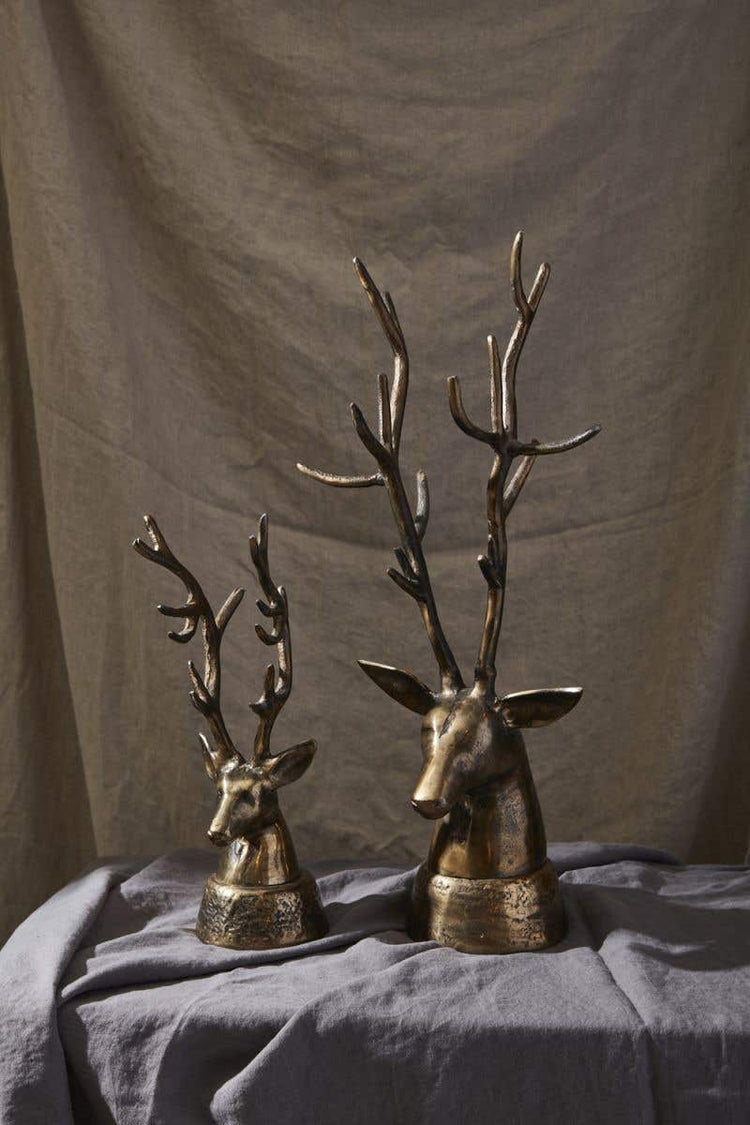 Two bronze-colored metal deer head sculptures with large antlers on a grey fabric surface.
