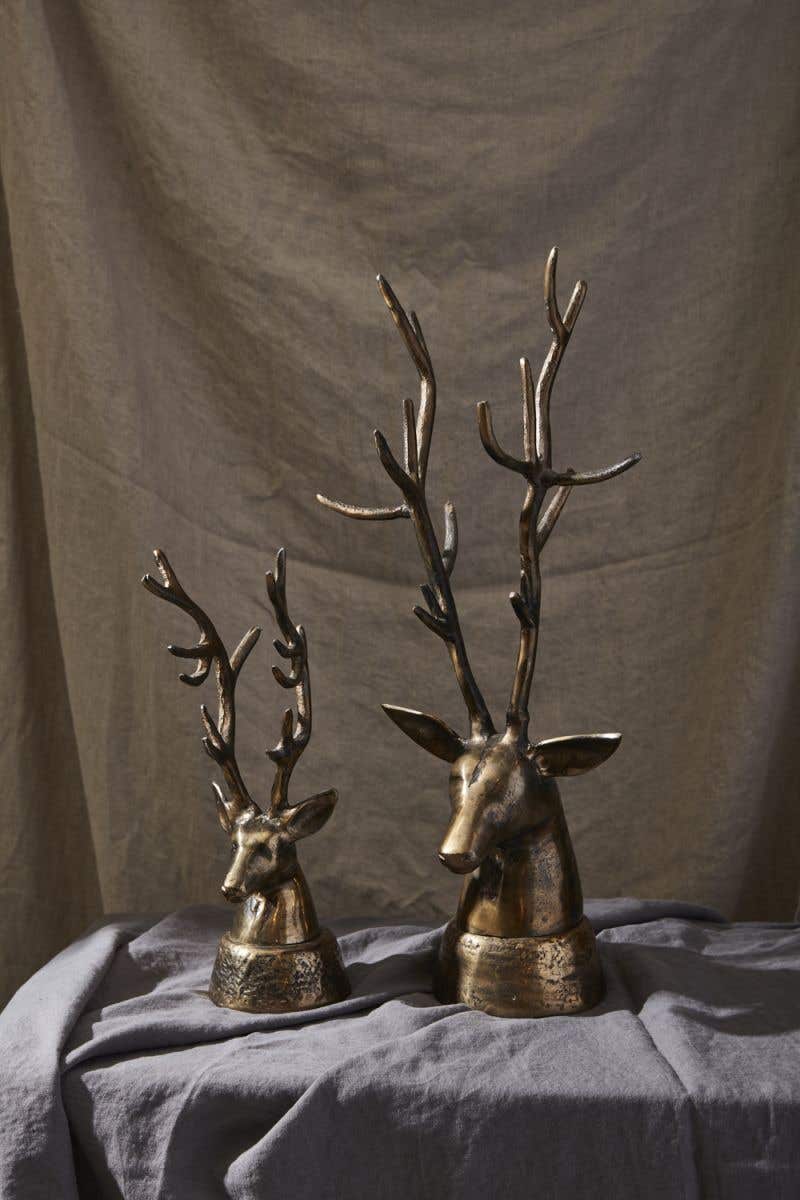 Two bronze-colored metal deer head sculptures with large antlers on a grey fabric surface.