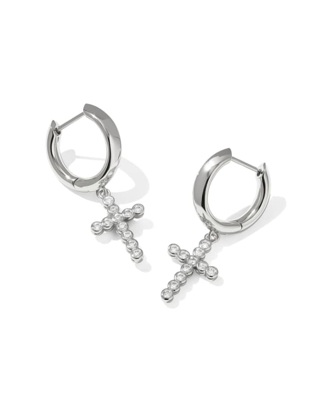 White cubic zirconia cross charm on a metallic huggie hoop earring.