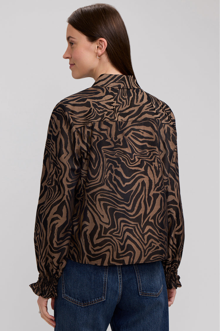Back view of a woman wearing the Vivienne Long Sleeve Zebra Shirt with ruffled cuffs and blue jeans.