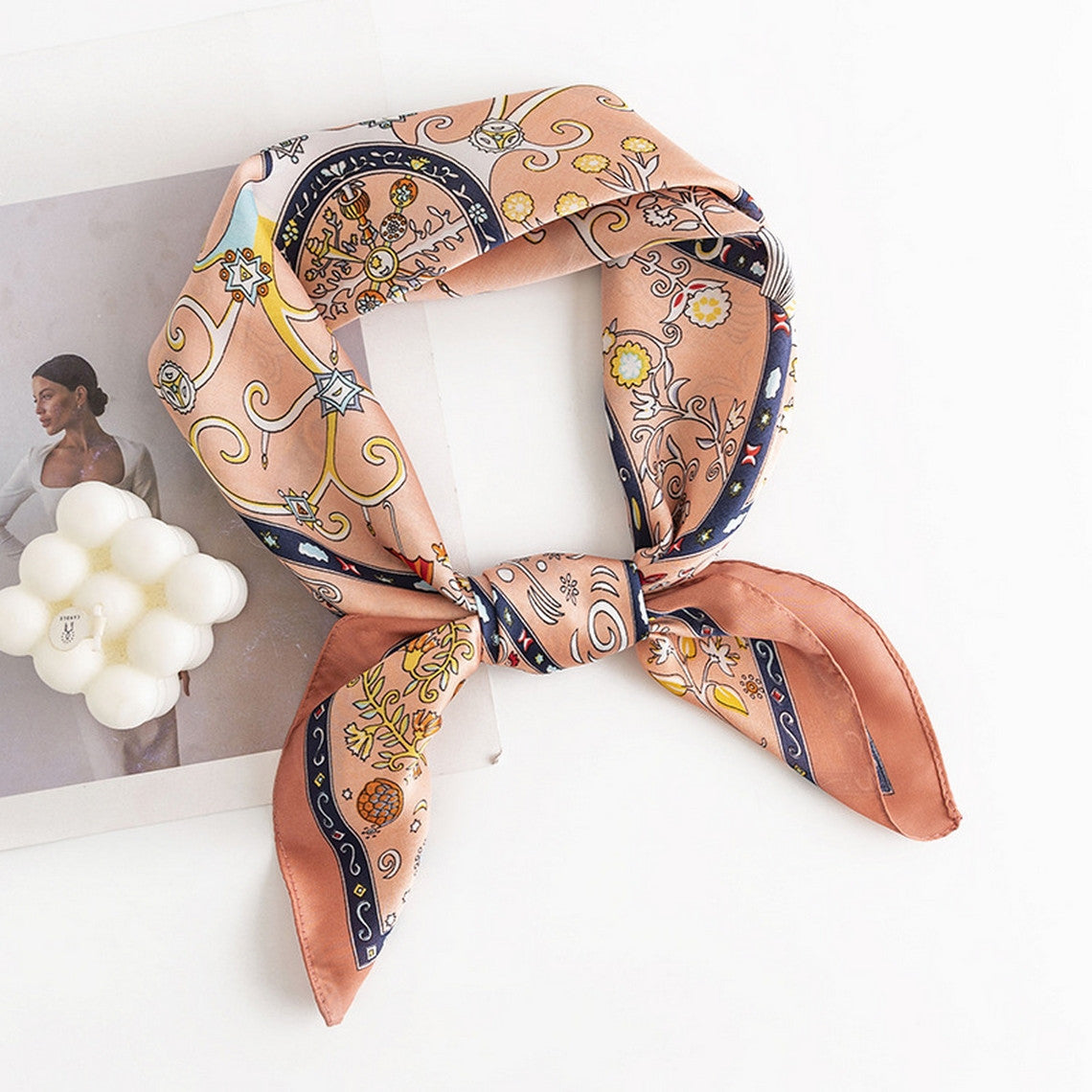 Peach floral satin square scarf tied in a knot, displayed on a white surface with a magazine.
