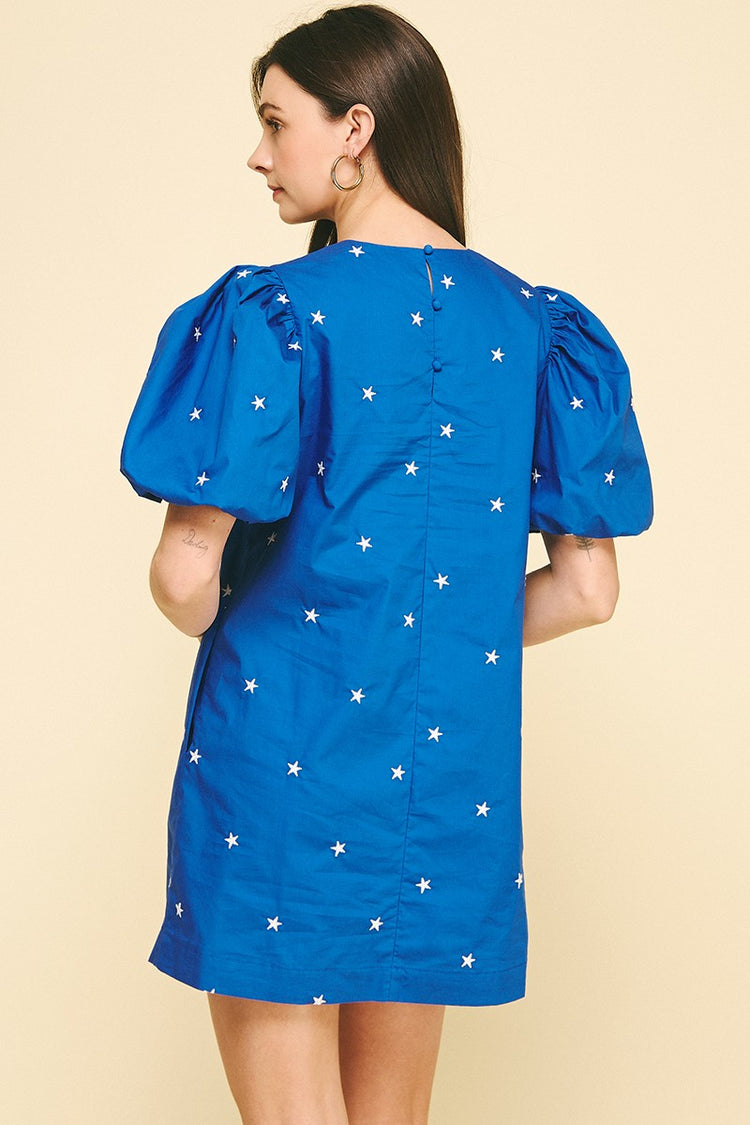 Back view of a blue cotton mini dress with white star embroidery and puff sleeves.