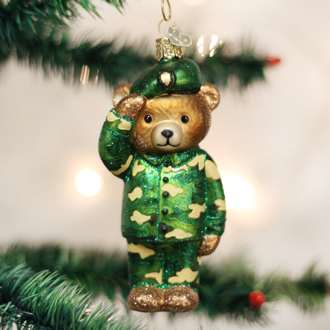 Glass Army Bear ornament in green camouflage uniform saluting on a Christmas tree branch.