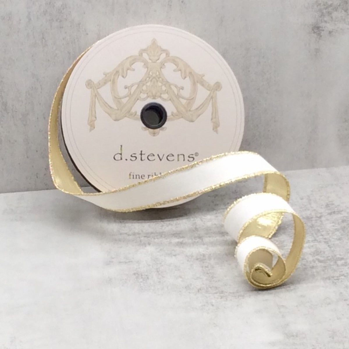 A spool of white flocked velvet ribbon with metallic gold edges on a grey background.