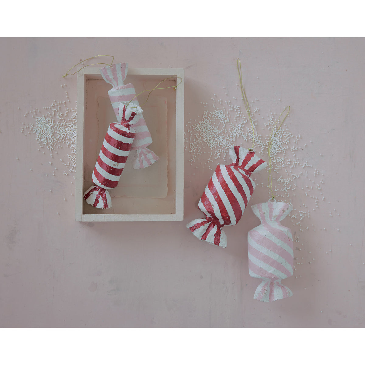 Handcrafted striped paper mache candy ornaments in red and pink, hanging on a pink background.