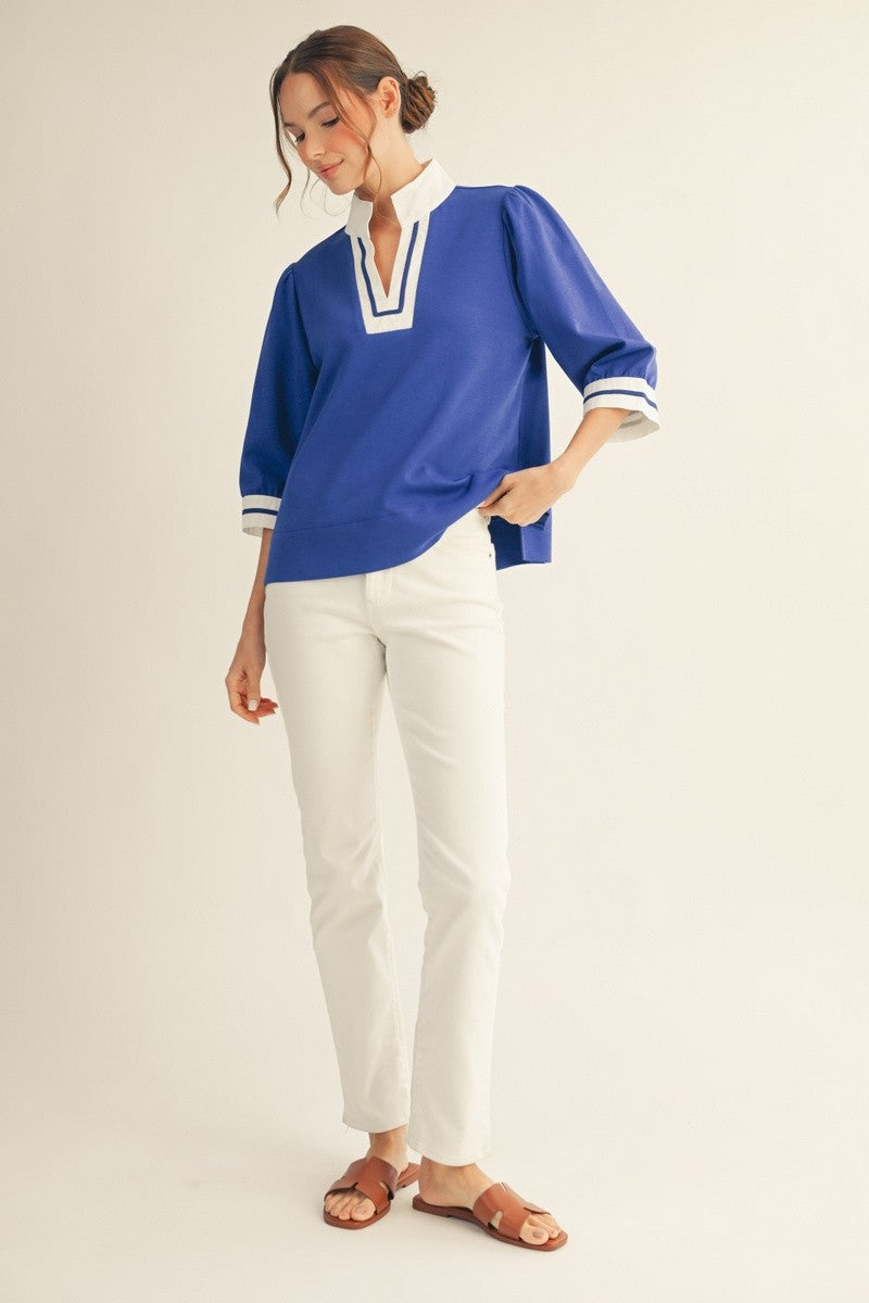 Solid top with standing neck, three-quarter sleeves, side slit hem, and color contrast accent detail.