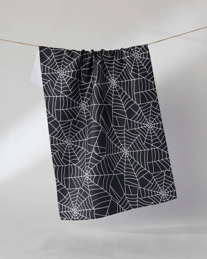 Black waffle weave tea towel with a white spiderweb pattern hanging on a string.