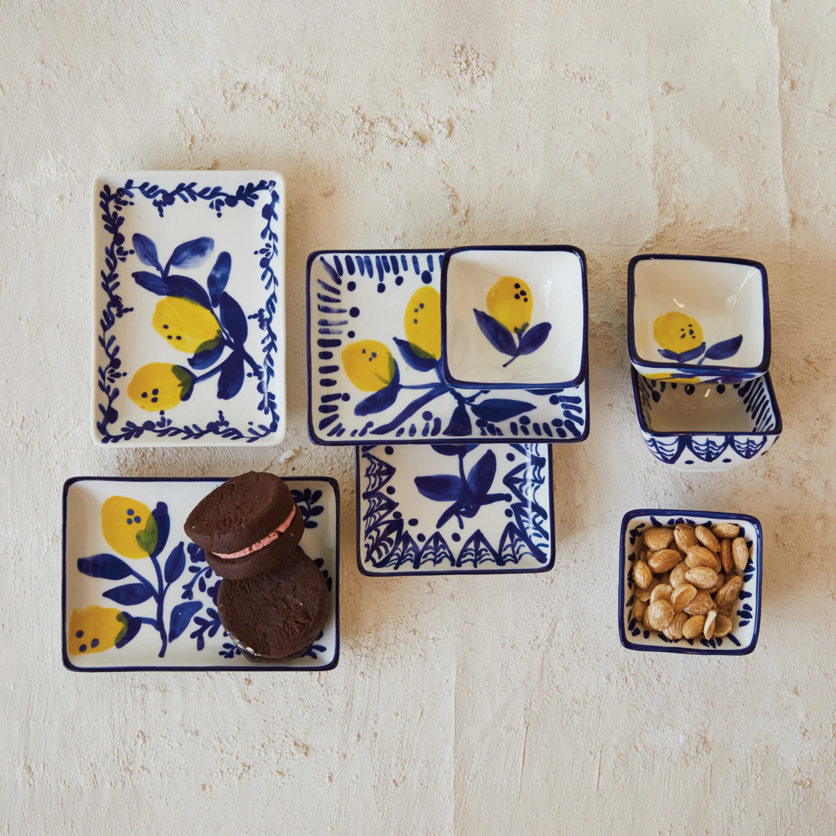 Hand-painted stoneware dishes with blue and yellow lemon designs, featuring cookies and nuts.