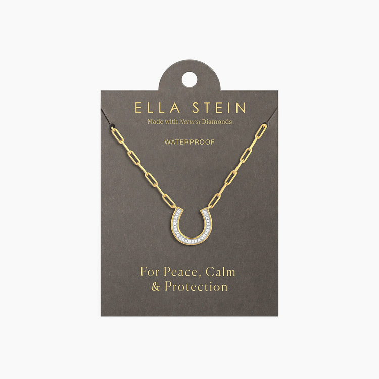 Gold horseshoe pendant necklace with diamonds on a paperclip chain, displayed on a grey card.