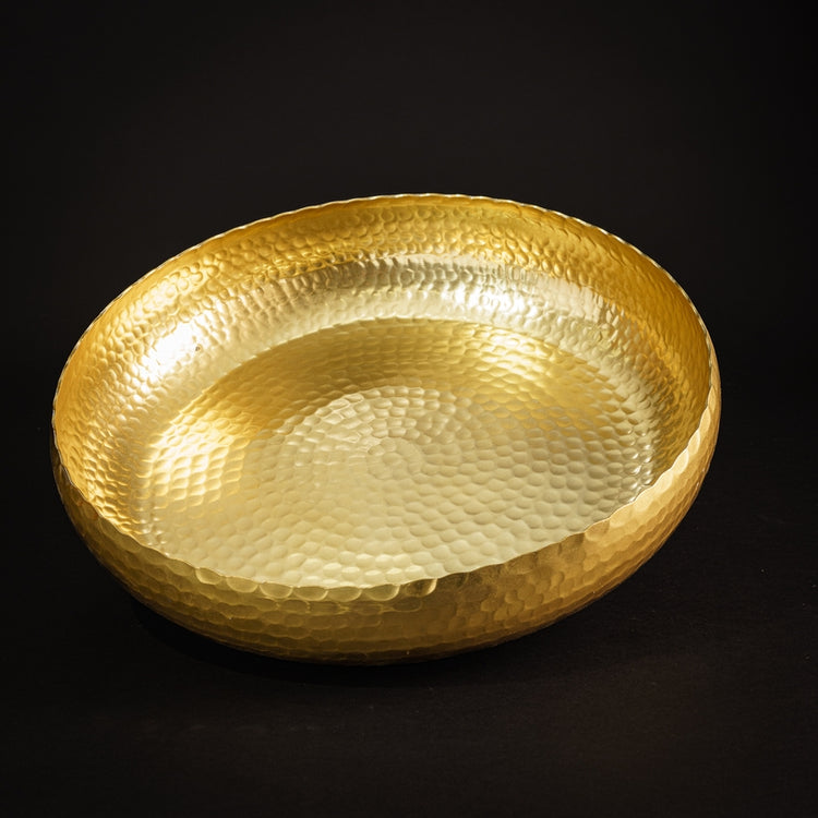 Round hammered gold-toned metal bowl with a textured surface on a black background.