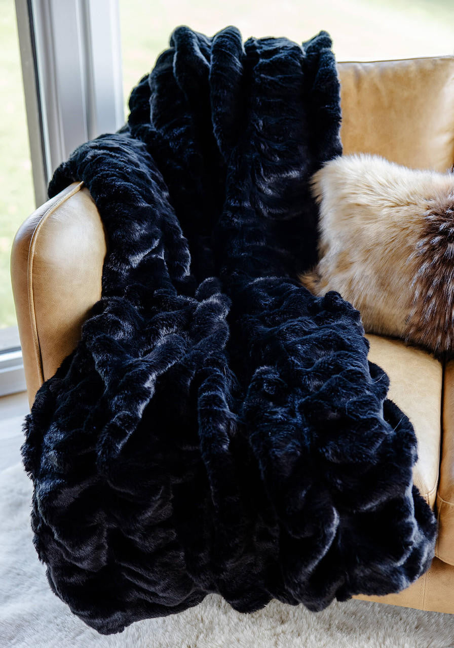Couture Throw Onyx Mink faux fur blanket draped over a tan leather chair.