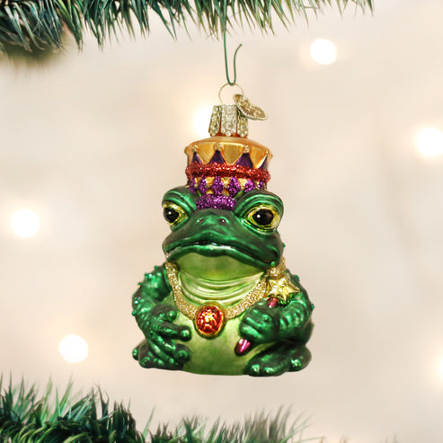 Green glass Frog King ornament with a glittery crown, gold necklace, and scepter on a tree.