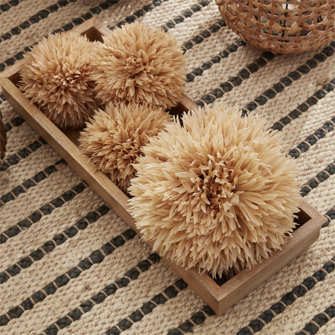 Four tan allium balls of varying sizes displayed in a rectangular wooden tray on a woven rug.