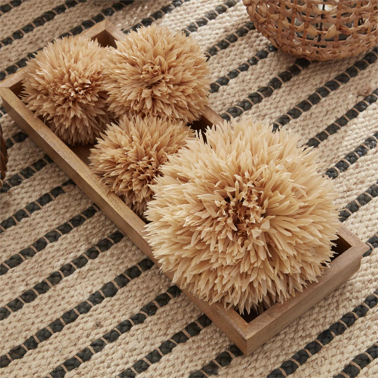 Four tan allium balls of varying sizes displayed in a rectangular wooden tray on a woven rug.