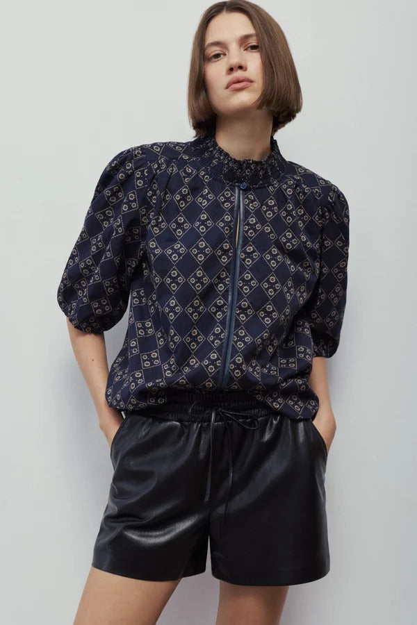 Woman wearing the Xena Blouse, a navy printed cotton top with a smocked mock neck and puff sleeves.