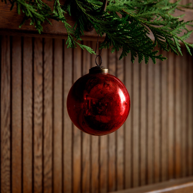 Vintage 4-inch red glass ball ornament with an antique finish hanging from a green garland.