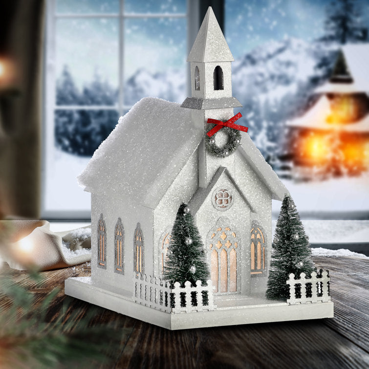 11.5-inch white sugared cardboard country church with LED lights, miniature trees, and a red bow.