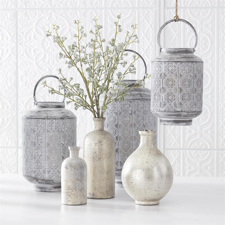 Whitewashed medallion punched metal lanterns and vases arranged against a white textured wall.